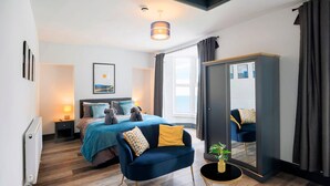 Een moderne slaapkamer met een bed, een bank, een klein tafeltje met een plant, een spiegel en een raam met gordijnen.