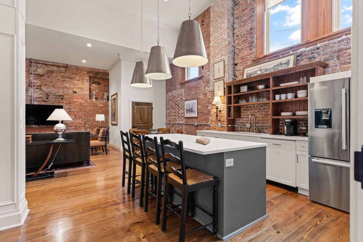 A modern kitchen with a brick wall, wooden flooring, and a central island with bar stools.