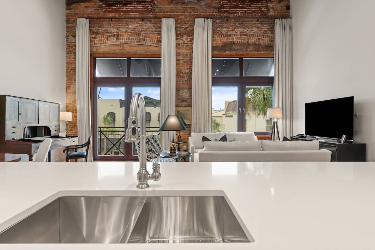 A modern kitchen with a large island, stainless steel sink, and a brick wall backdrop.