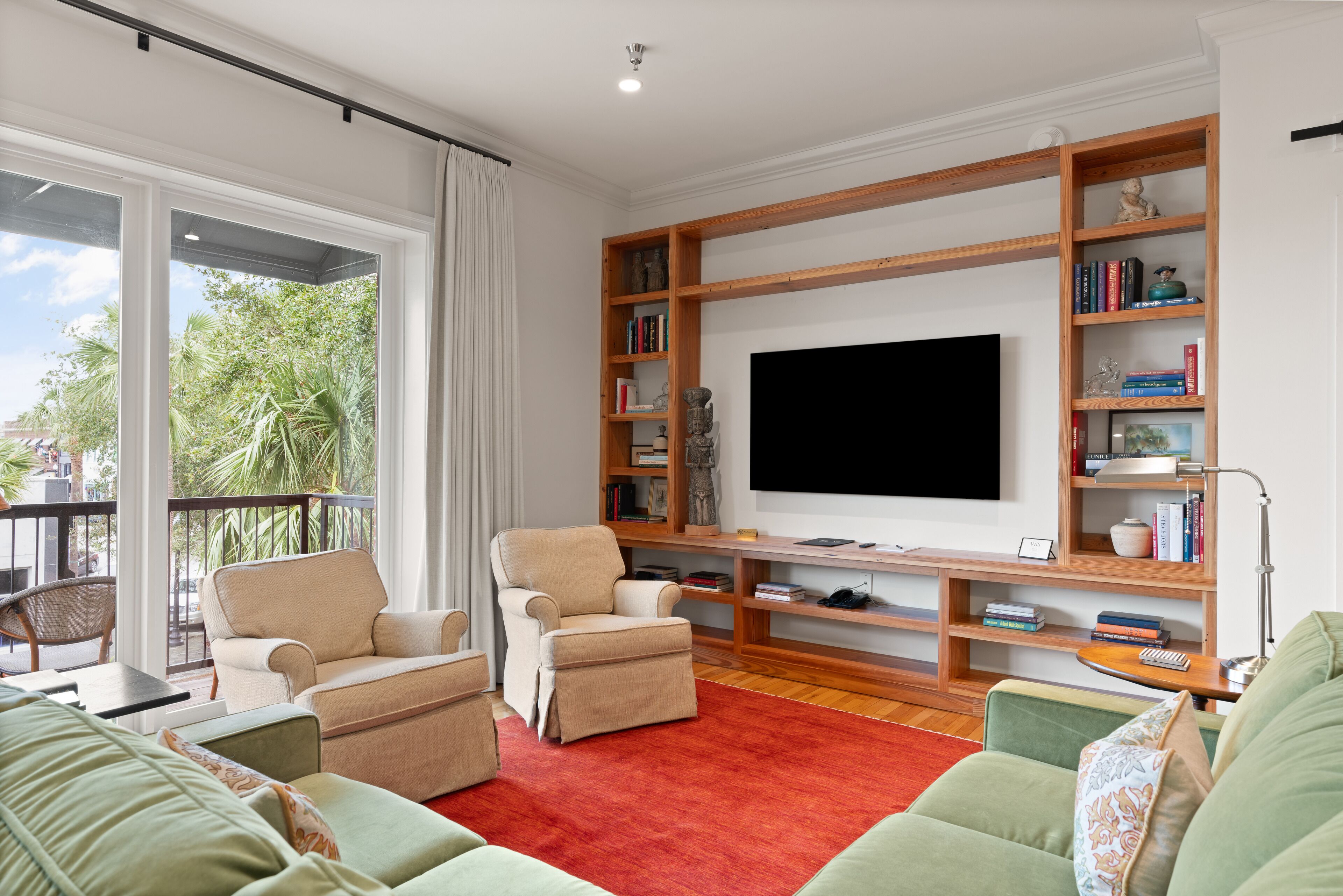 A living room with a large flat-screen TV, a wooden bookshelf, and a red carpet.
