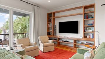 A living room with a large flat-screen TV, a wooden bookshelf, and a red carpet.