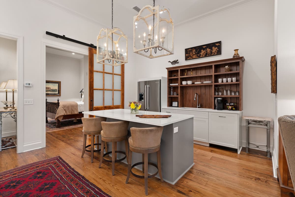 A modern kitchen with a central island, bar stools, a refrigerator, and a wooden cabinet with shelves.