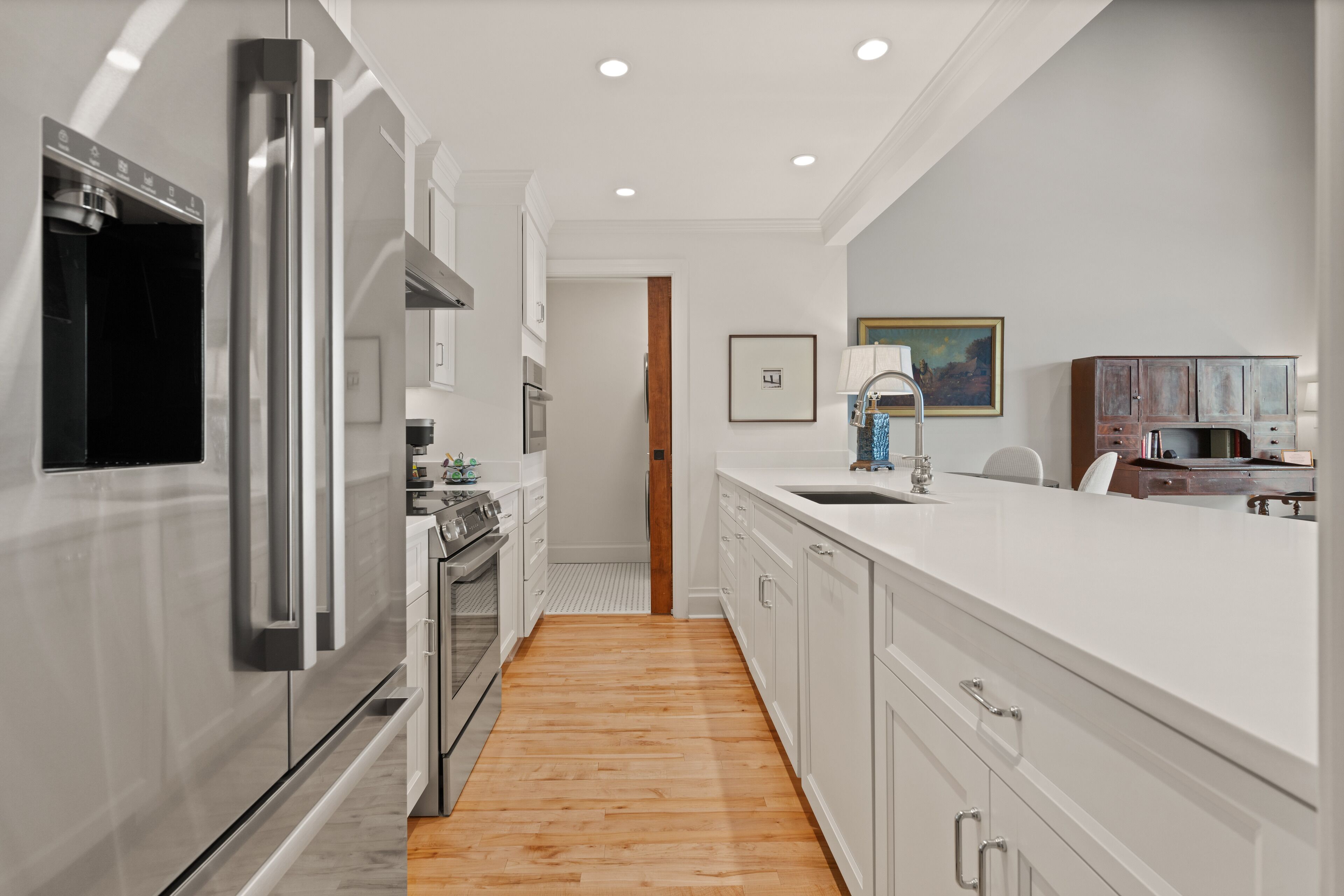 Una cocina moderna con electrodomésticos de acero inoxidable, armarios blancos y piso de madera.