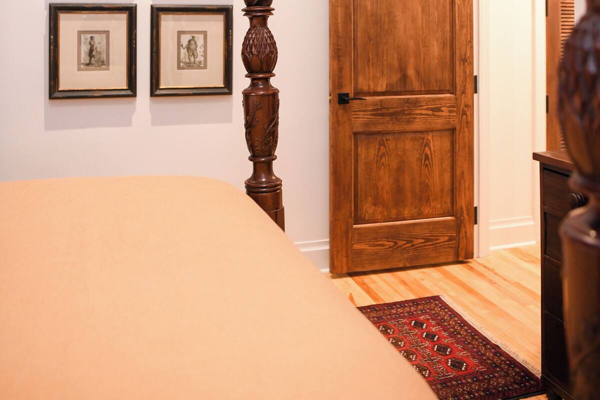 A bedroom with a bed, a wooden floor, a door, and four framed pictures on the wall.
