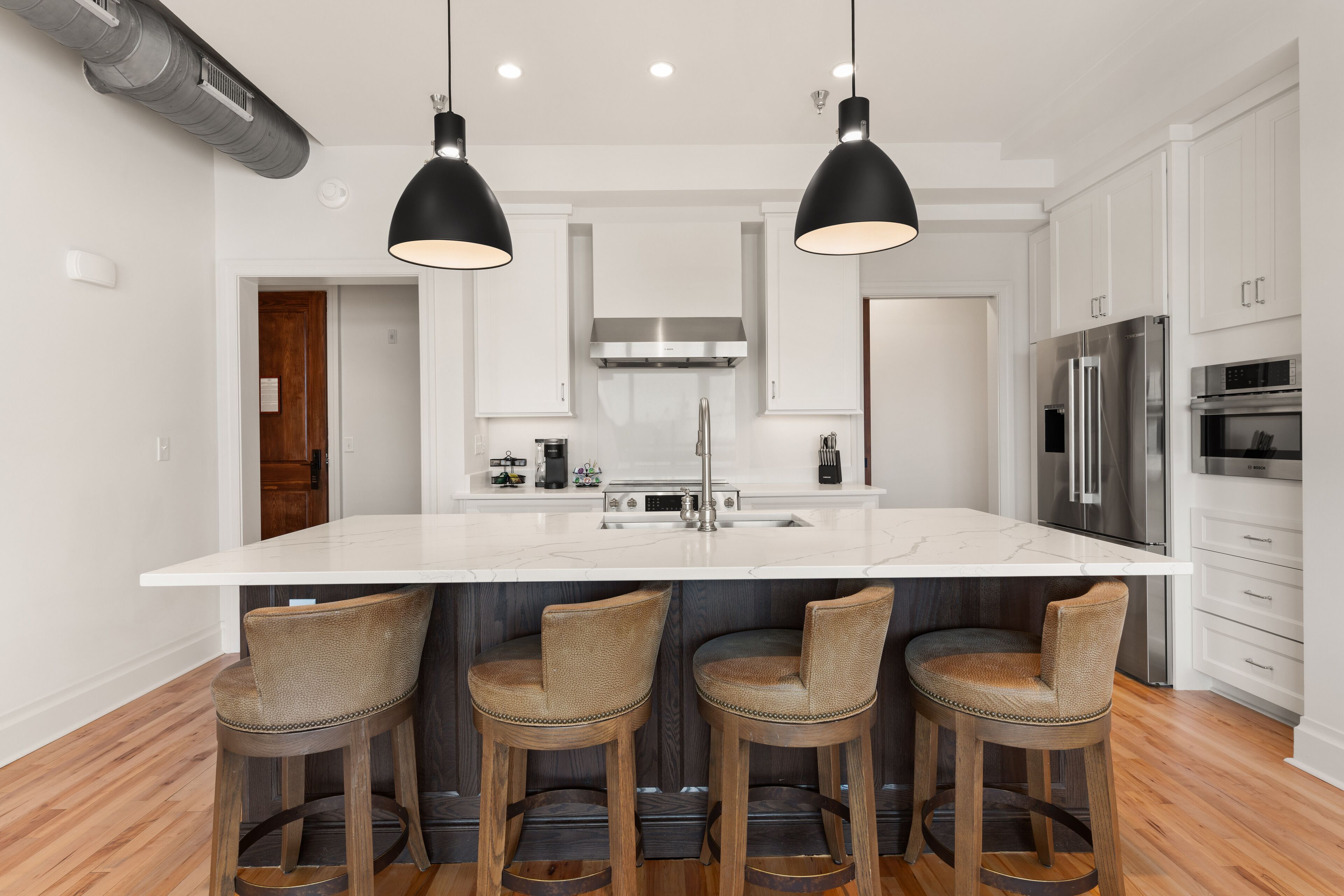 Una cocina moderna con una isla grande, taburetes de bar, electrodomésticos de acero inoxidable e iluminación colgante.