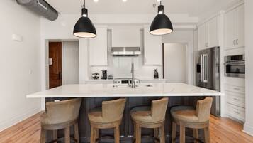 Una cocina moderna con una isla grande, taburetes de bar, electrodomésticos de acero inoxidable e iluminación colgante.
