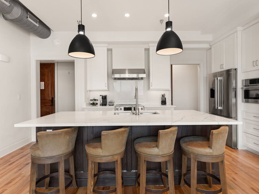 Una cocina moderna con una isla grande, taburetes de bar, electrodomésticos de acero inoxidable e iluminación colgante.