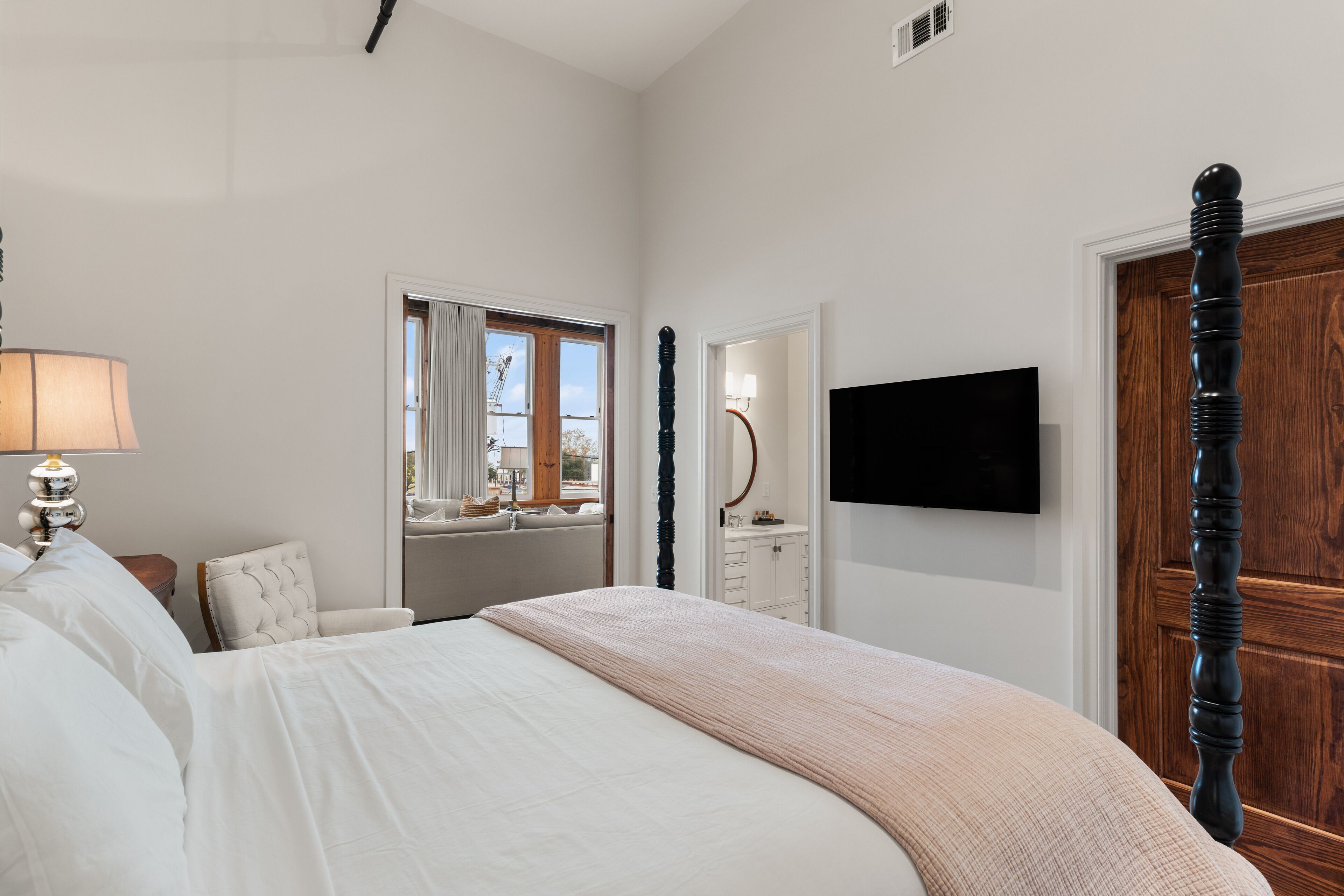 A bedroom with a bed, a bedside lamp, a window, a dresser, a mirror, and a television.