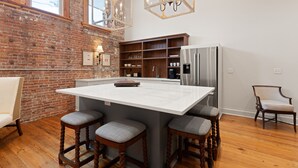 A kitchen with a large island, wooden bar stools, a refrigerator, and a brick wall. - The Kress Brunswick (Brunswick)
