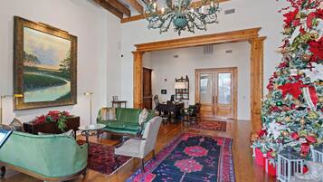 A spacious living room with a large painting, a green sofa, a wooden coffee table, and a Christmas tree.