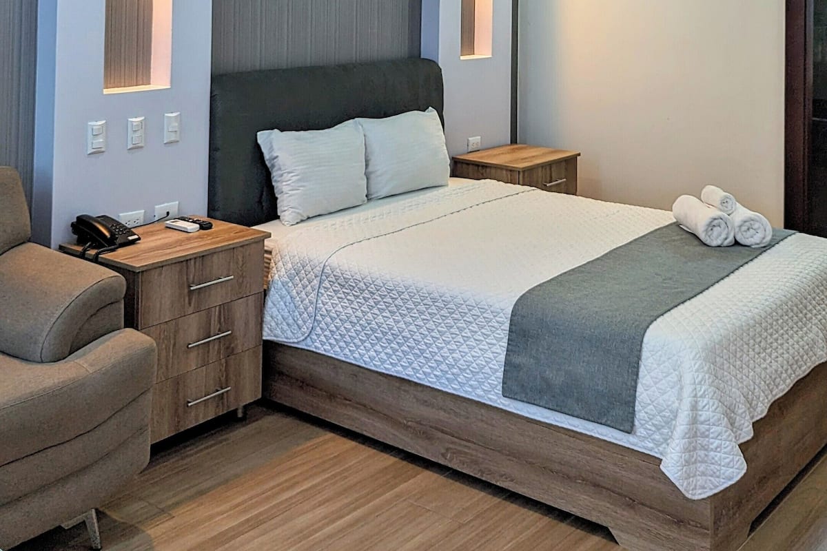 Ein modernes Schlafzimmer mit Bett, Nachttischen, einem Sessel und integrierter Beleuchtung.