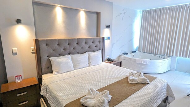 Quarto de hotel moderno com cama grande, banheiro separado com hidromassagem e vista para o horizonte urbano.