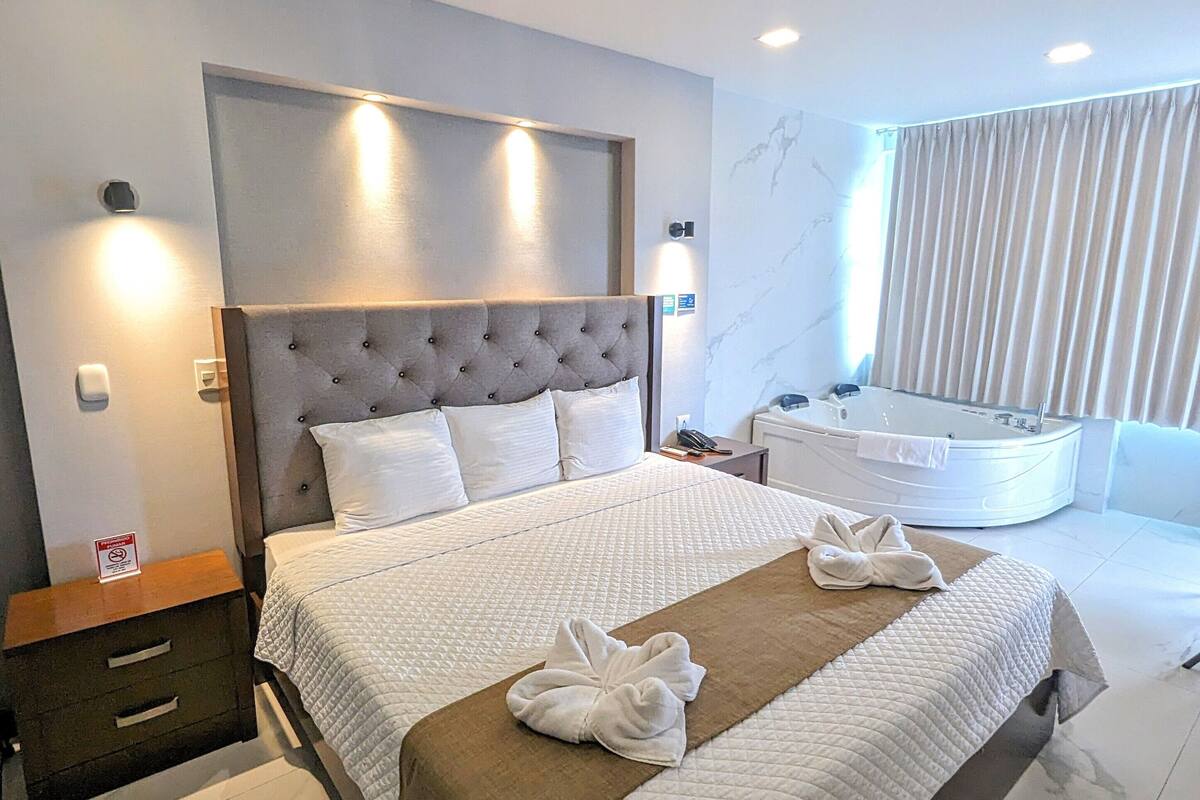 Ein modernes Hotelzimmer mit einem großen Bett, einem eigenen Badezimmer mit Whirlwanne und Blick auf die Stadtlandschaft.