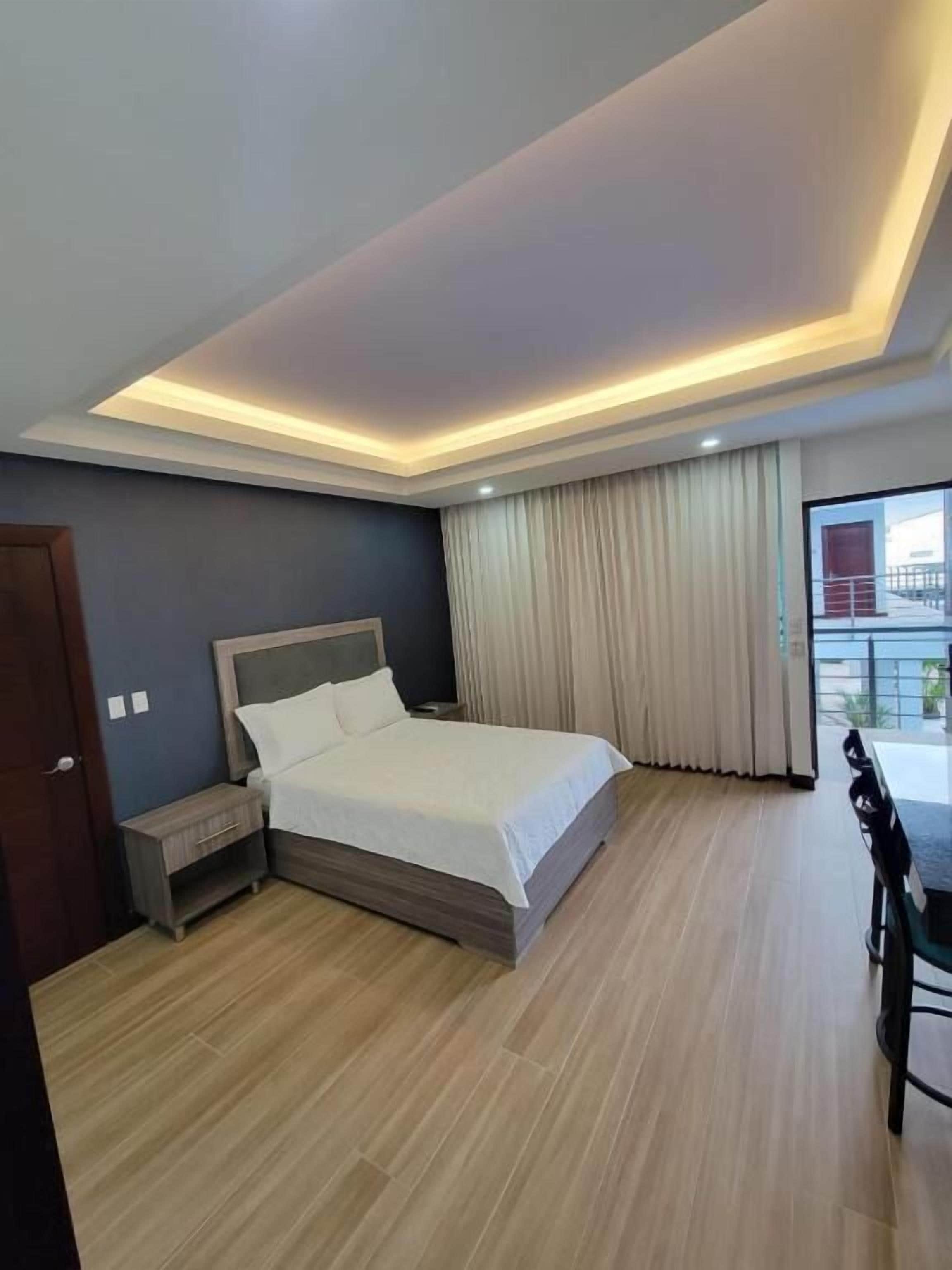 A modern bedroom with a large bed, bedside tables, a wooden floor, and a view through a large window.