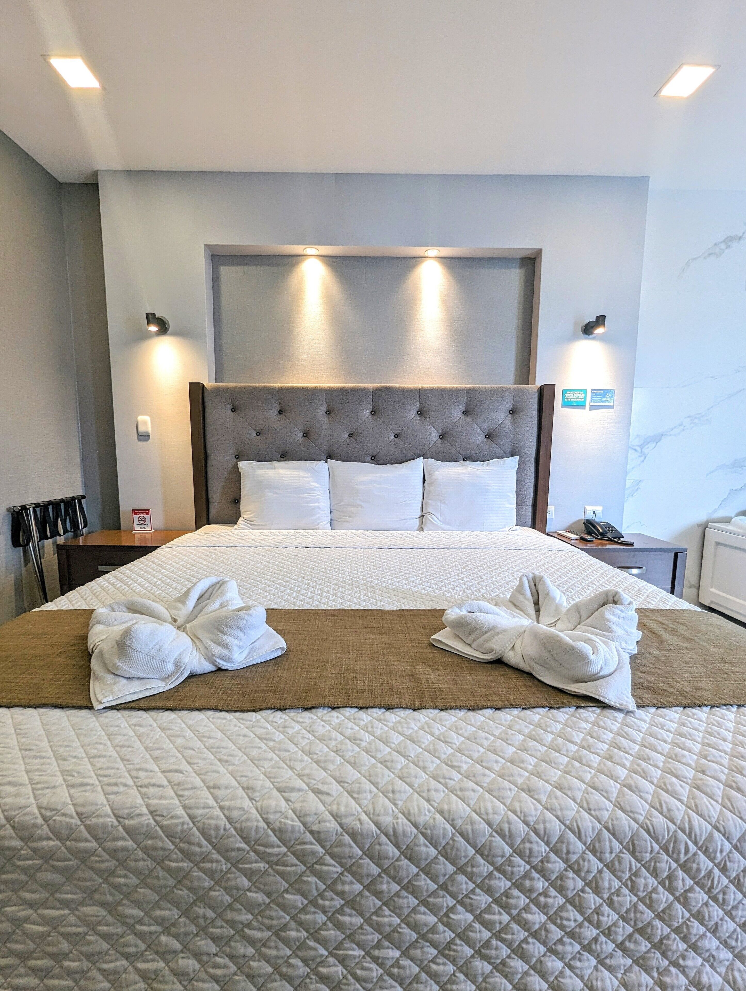 Hotelkamer met een groot bed, een hoofdbord met ingebouwde verlichting, een nachtkastje met telefoon en een wandlamp.