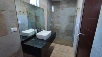 A bathroom with two white sinks, a black countertop, a mirror, and a shower area.
