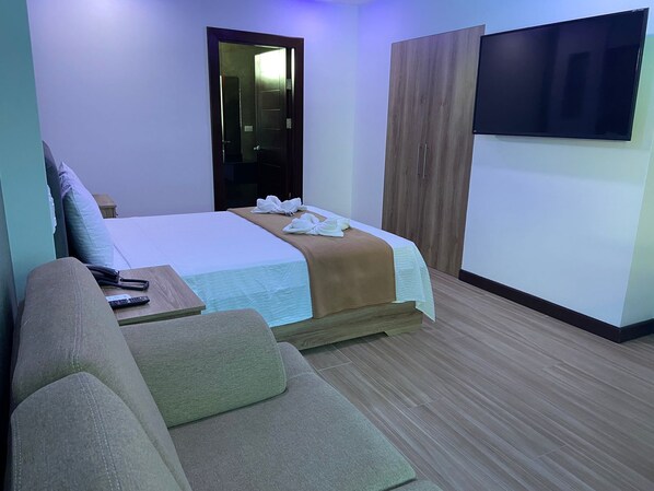 A hotel room with a bed, a TV, a wardrobe, and a sofa.