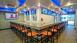 Uma área de bar com um balcão extenso, várias telas de TV e muitos bancos altos.