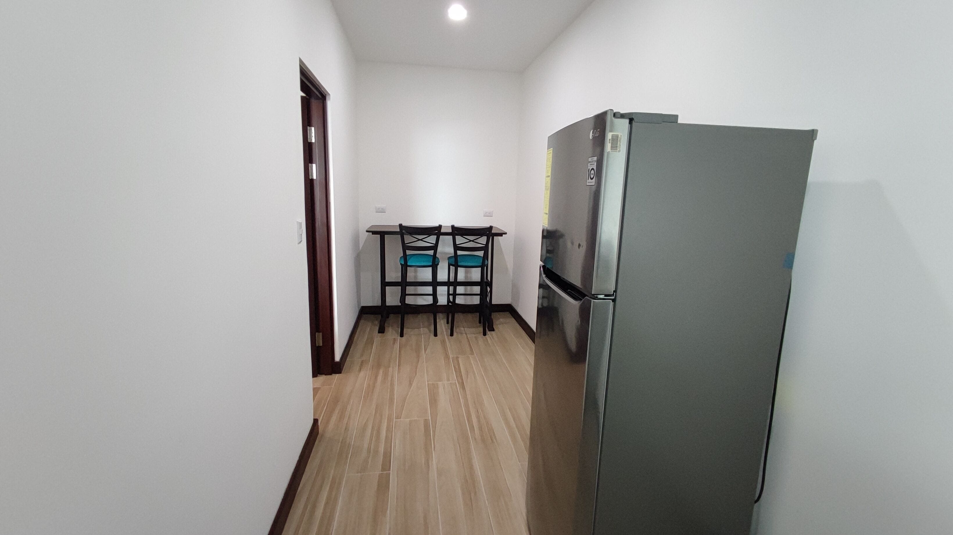 A narrow hallway with a kitchen area featuring a refrigerator and a table with chairs.