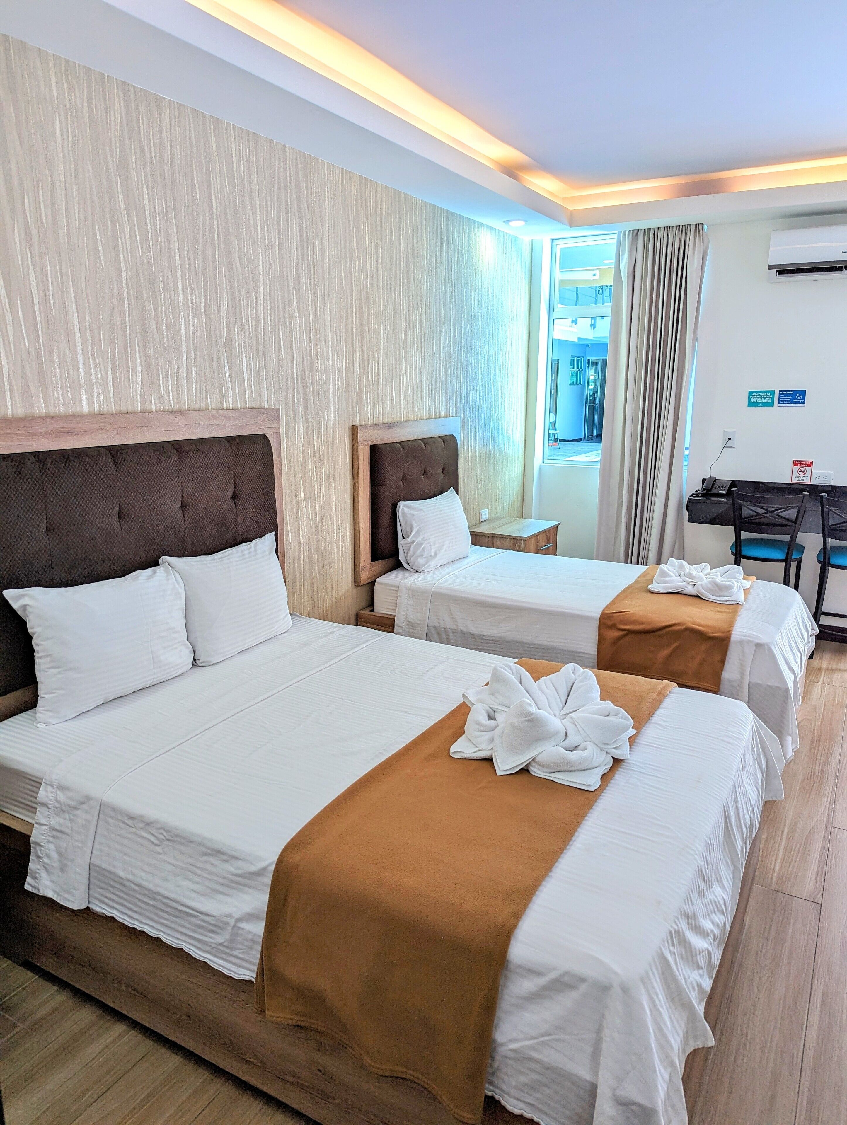 A hotel room with two beds, a desk, and an air conditioning unit.