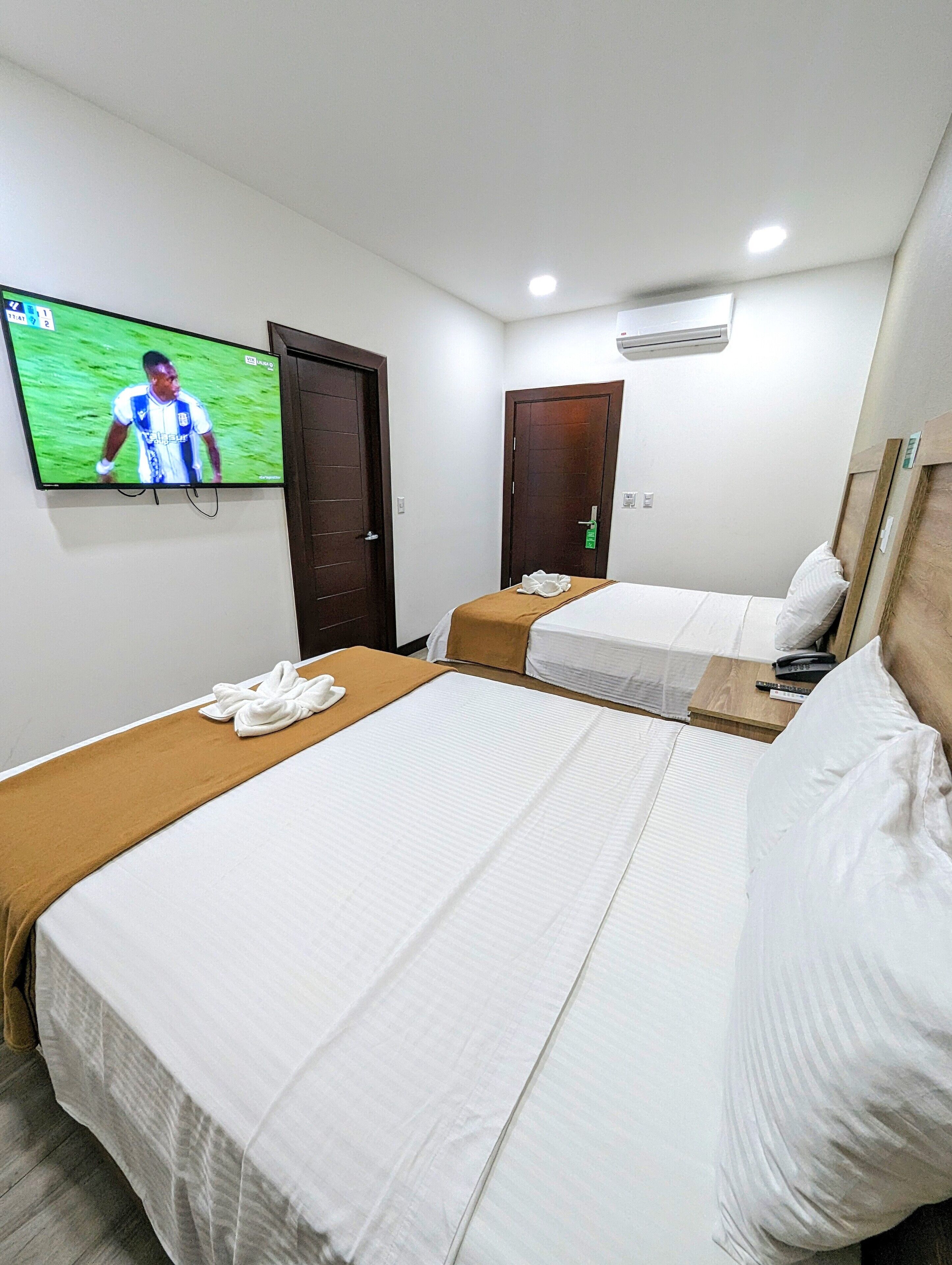 Een hotelkamer met twee bedden, een aan de muur bevestigde televisie en een deur.
