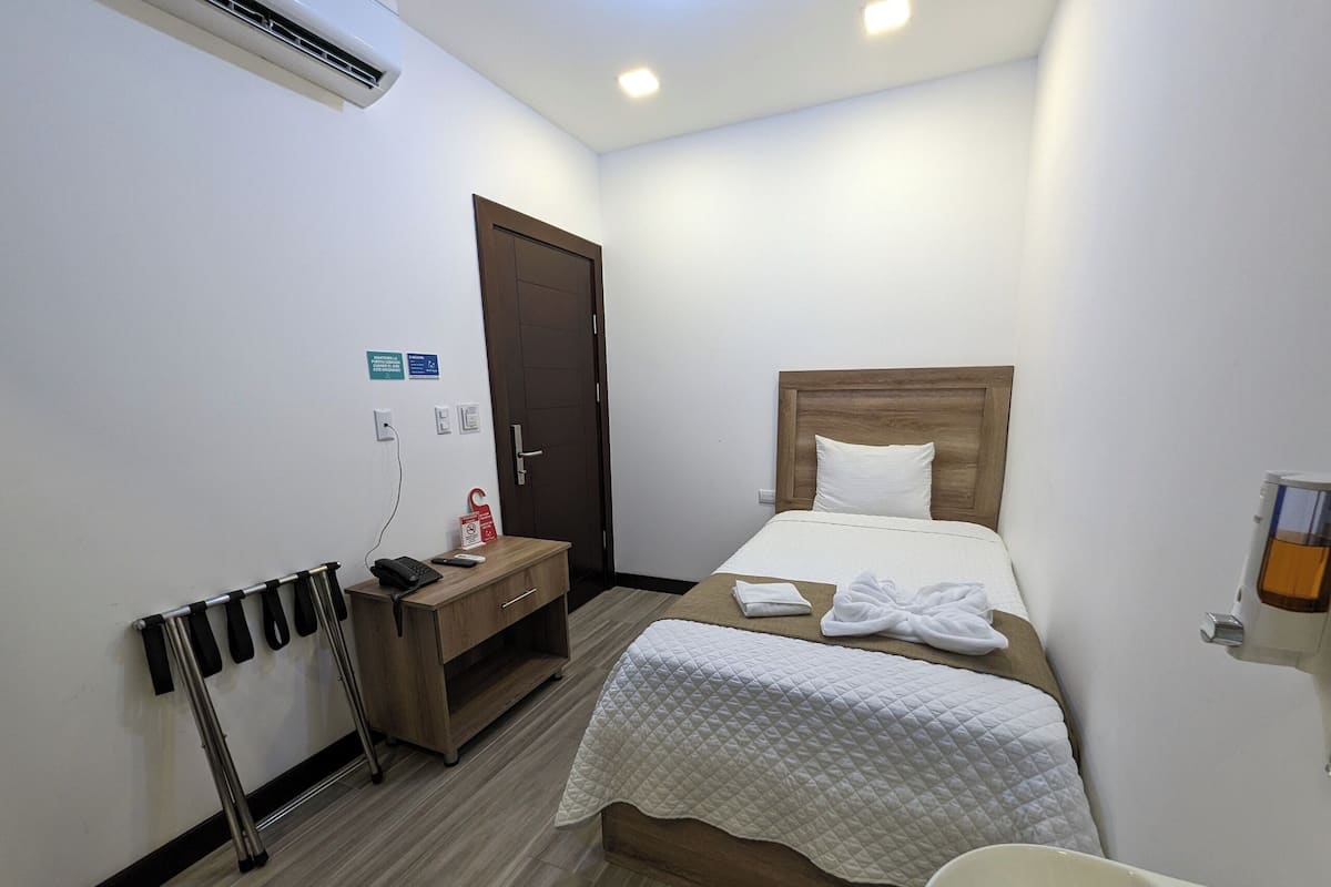 Ein Hotelzimmer mit Bett, Nachttisch und Schreibtisch mit Stuhl. Ein Kleiderständer und ein Badezimmerspiegel sind ebenfalls vorhanden.