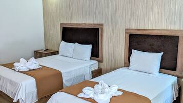Quarto de hotel com duas camas, cabeceiras de madeira, roupa de cama branca e um cobertor marrom.