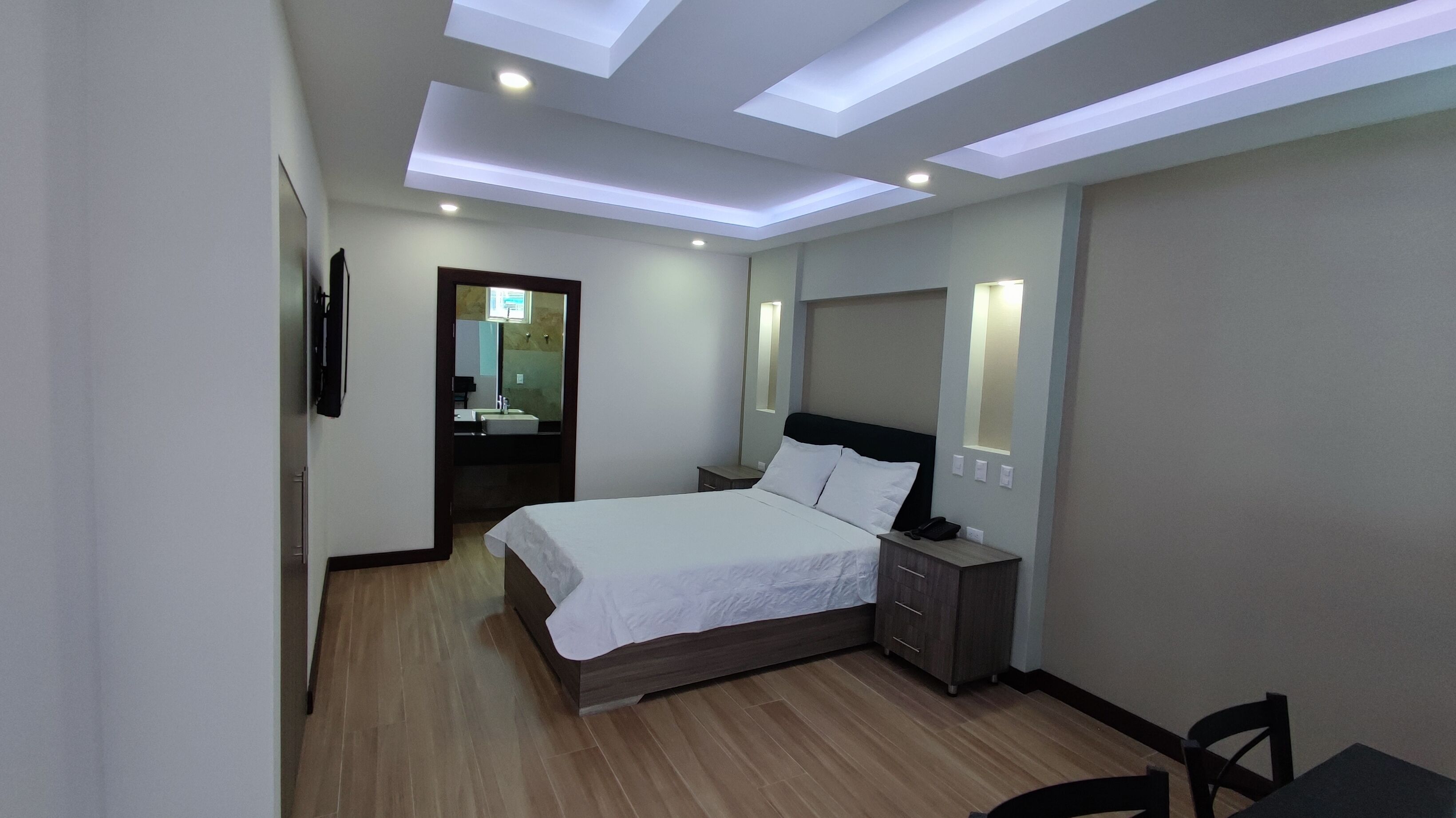 A modern hotel room with a large bed, bedside tables, a desk, and a mirror.