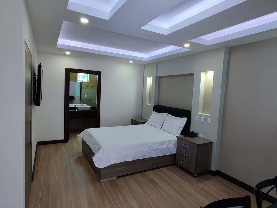 A modern hotel room with a large bed, bedside tables, a desk, and a mirror.