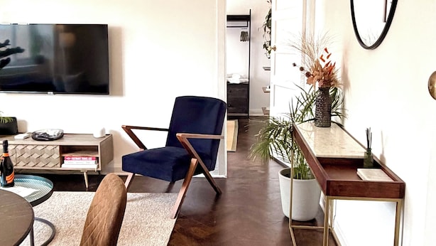 Un soggiorno moderno con una televisione a schermo piatto, una poltrona blu, un tavolino in legno e un'area pranzo con una sedia marrone.