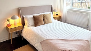 Una camera da letto ordinata con un letto grande, due comodini con lampade, una finestra con tende e un termosifone.