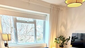 Zona pranzo con tavolo rotondo apparecchiato per quattro persone, un divano blu sullo sfondo e un televisore su un mobile.