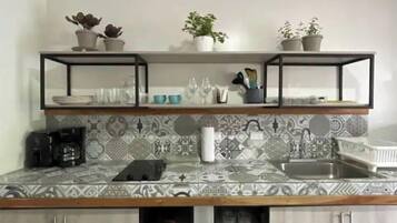 Een keuken met een decoratieve spatwand, een koffieapparaat, een gootsteen en kasten.