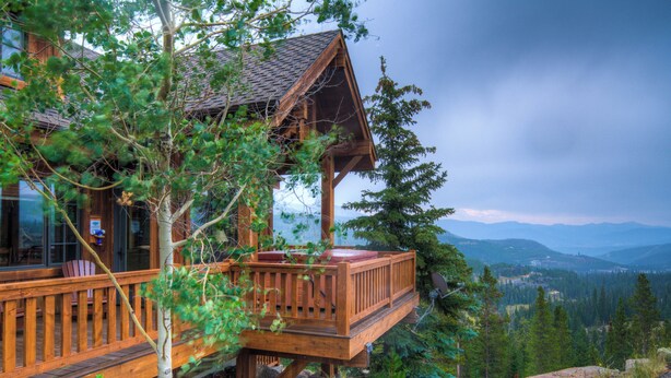 Eine Holzhütte mit einer Terrasse, umgeben von Bäumen und Bergen.
