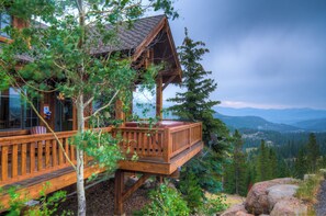 A wooden cabin with a deck, surrounded by trees and mountains. - Silverstar Chalet Ski IN/Out Hot Tub (Big Sky)