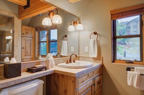 Un baño con muebles de madera, un espejo grande, un lavamanos con grifo y toallas colgadas.