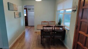 A narrow hallway with a dining table and chairs, a wooden door, and a window.