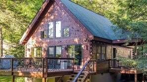 Cozy cabin with a gabled roof and deck area, featuring multiple windows and outdoor seating.