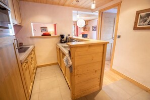 A compact kitchen with wooden cabinets, a built-in oven, and a small countertop. - Chantemerle 6 ski-in / ski-out route des Chalets (Les Allues)