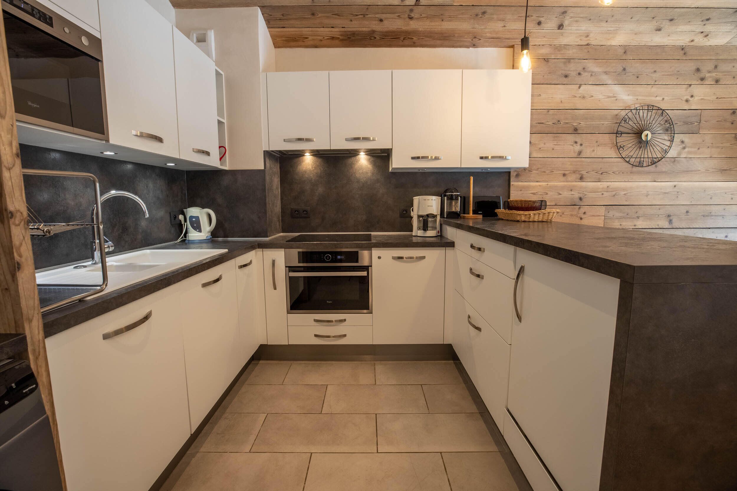 A modern kitchen with white cabinets, a built-in oven, a coffee maker, and a wooden wall panel.