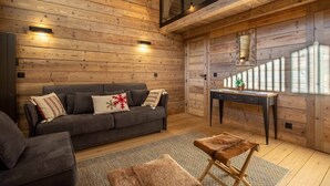 A cozy log cabin interior with a dark gray sofa, a small wooden table, and a fur-covered ottoman. - Sherpa 17 spacious apartment with sauna (Les Allues)
