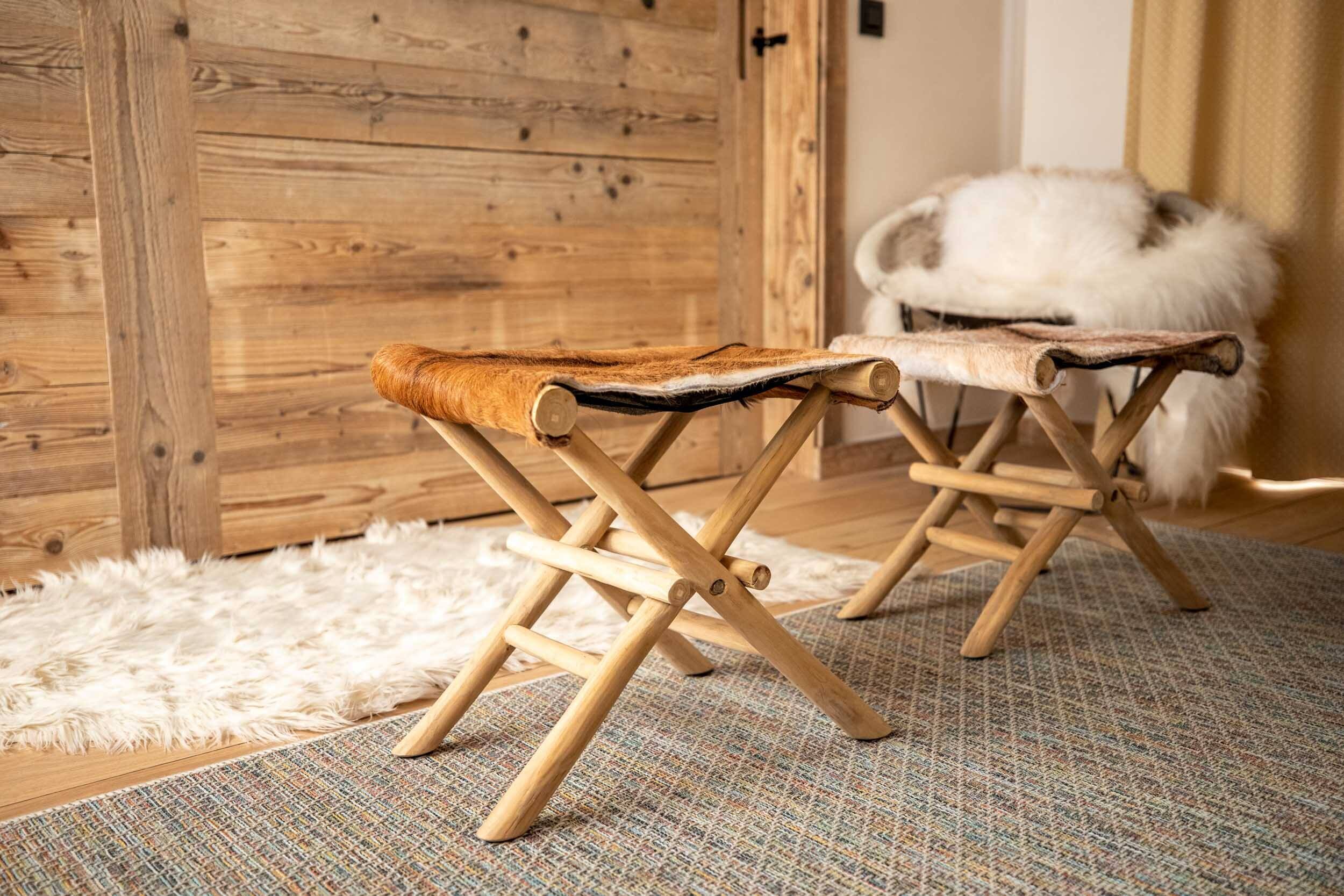A wooden folding chair with a fur seat and backrest, placed on a patterned rug in a room with a wooden door and a fluffy white rug.
