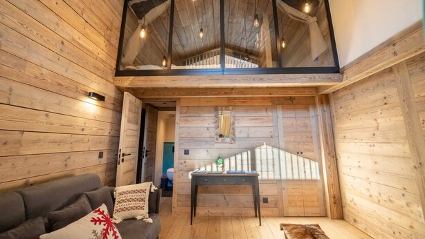A wooden interior with a loft bedroom, a sofa, a table, and a staircase. - Sherpa 17 spacious apartment with sauna (Les Allues)