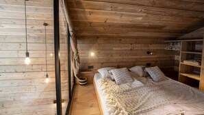 A cozy bedroom with wooden walls and ceiling, a bed with a white blanket, and a small bedside table with a lamp. - Sherpa 17 spacious apartment with sauna (Les Allues)