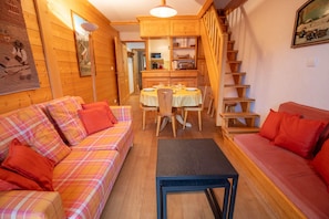 Um quarto acolhedor com um sofá xadrez, uma pequena mesa e uma escada que dá para uma área de cozinha.