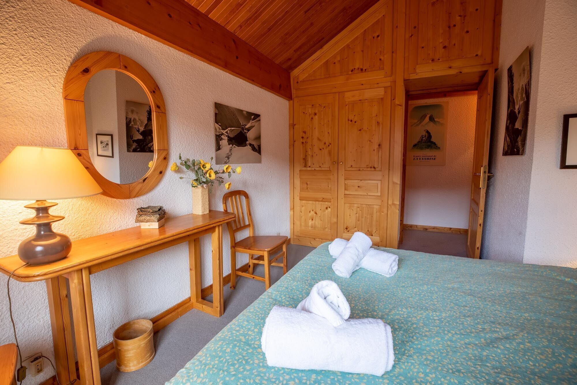 Ein gemütliches Zimmer mit einem Holztisch, einem Stuhl, einem Bett mit Handtüchern, einem Spiegel und Holzwänden.