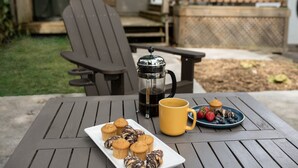 A patio with a table set for breakfast, including a coffee pot, a yellow mug, a plate of muffins, and a plate of fruit. - Quiet and Modern Designed Cottage in St Paul (St. Paul)