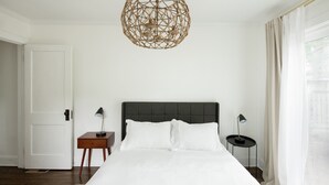 A bedroom with a large bed, two bedside tables, a decorative ceiling light, and a view through a window. - Quiet and Modern Designed Cottage in St Paul (St. Paul)