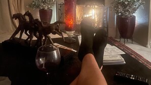 Uma sala de estar com lareira, uma televisão fixada acima dela e uma mesa com uma taça de vinho e um controle remoto.