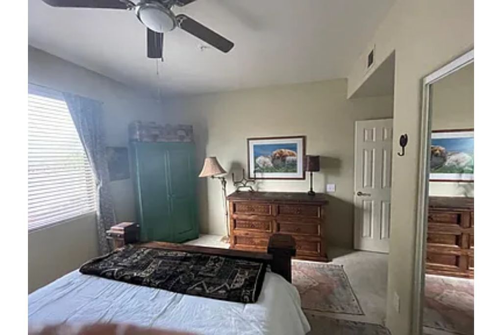A bedroom with a bed, a dresser, a ceiling fan, and a door leading to another room.